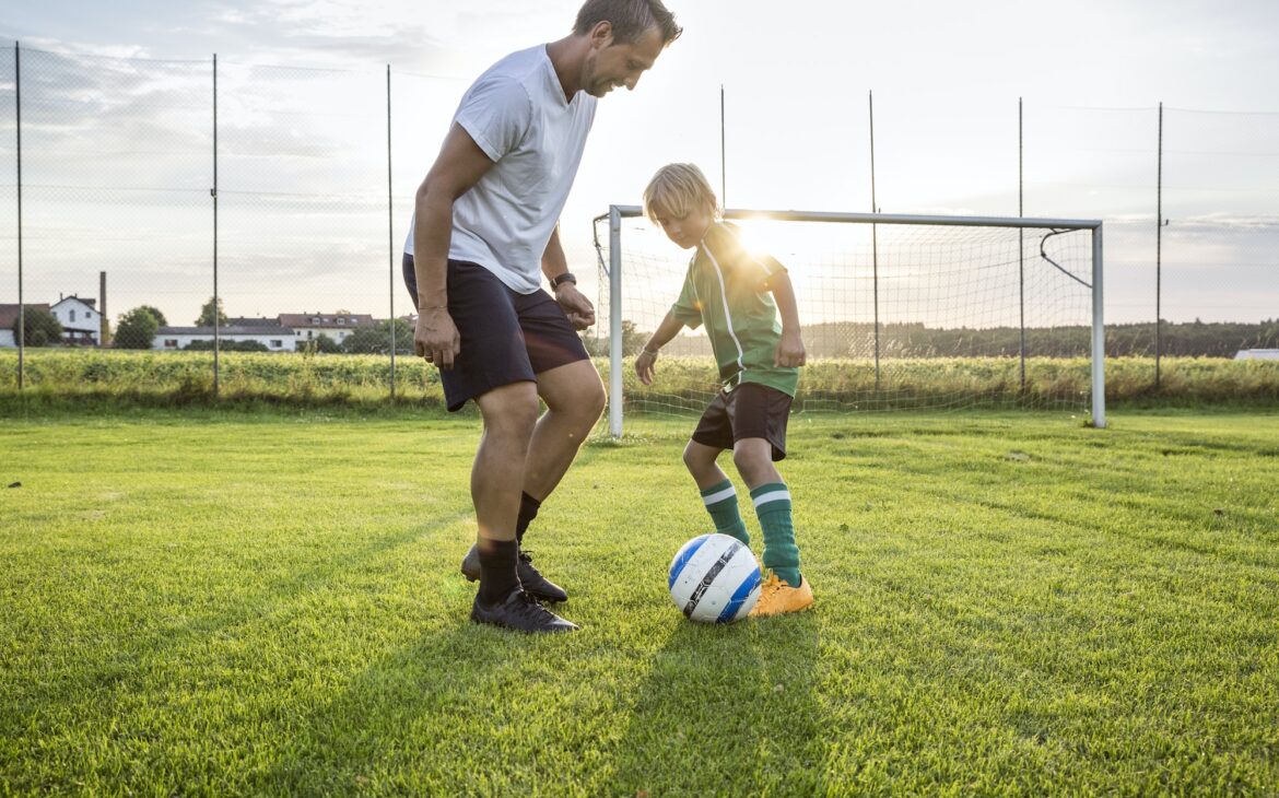 Coach and young football player on football ground at sunset